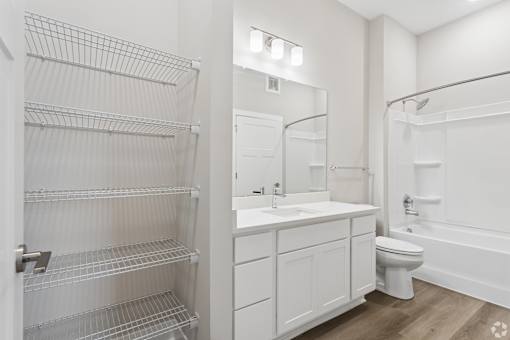 Bathroom with quartz countertops, closet, and bath/shower of an apartment unit.