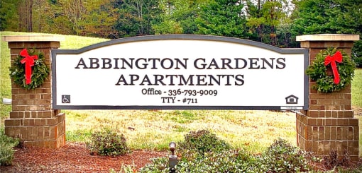 A sign for Abbington Gardens Apartments is displayed in front of a green area.