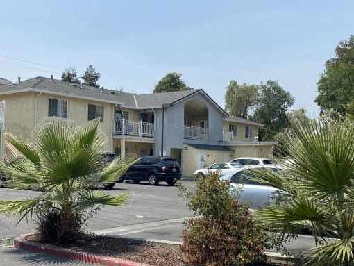 a large apartment complex with palm trees in the foreground and a parking lot in the background