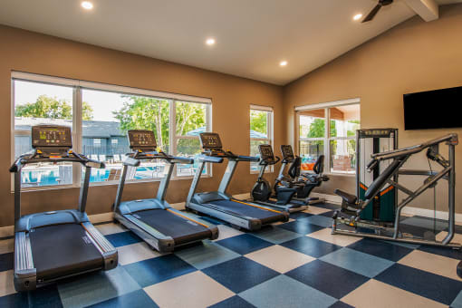 a gym with cardio equipment and a large window with a view of the pool