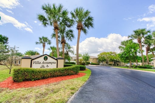 Drive into Villa Assumpta with monument signage with shrubs and palm trees