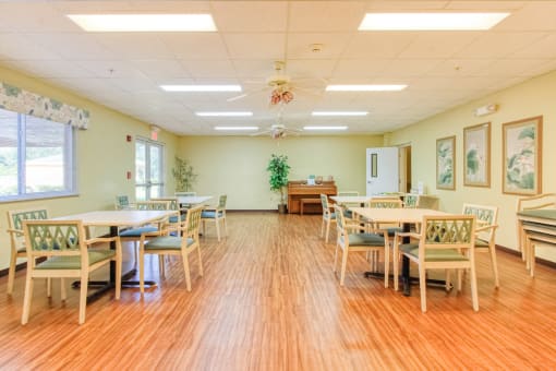 Community room with tables, chairs, piano, and plenty of light