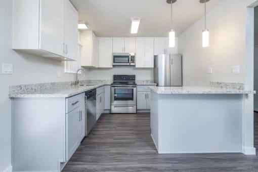 Alternate view of kitchen with stone counters, white cabinets, stainless appliances