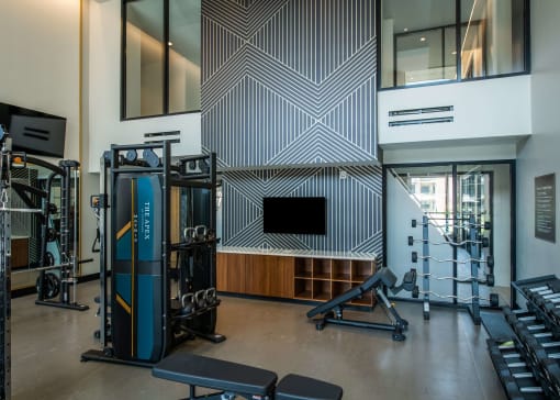 indoor workout room with a tv, free weights, and cables with benches at The Apex at CityPlace, Overland Park, 66210