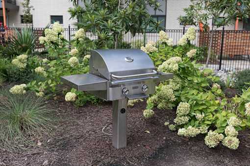 A silver barbecue grill is in the middle of a garden.