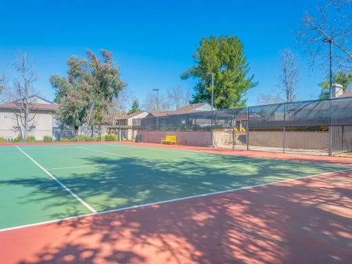 a tennis court with a fence and houses in the background
