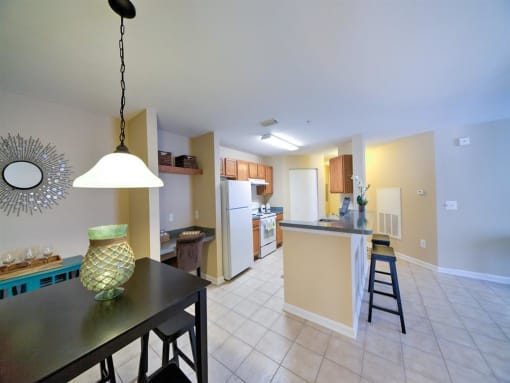 Kitchen with white appliances, breakfast bar, dining room table with pendant lighting, and tile flooring