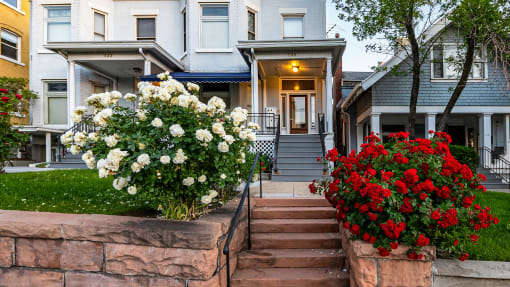 Front exterior of light blue First Avenue Home with flower bushes
