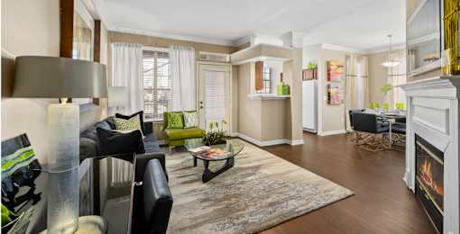 Spacious living room and dining room with wood-burning fireplace with glass doors, ceiling fan, 9-foot ceilings and wood grain plank flooring at The Lanesborough Apartments in Houston.