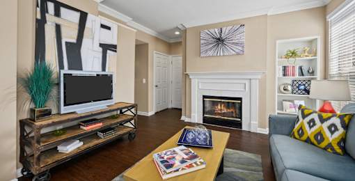 Spacious living room with wood-burning fireplace with glass doors, 9-foot ceilings, built-in shelves, and wood grain plank flooring at The Lanesborough Apartments in Houston.