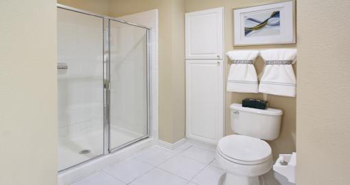 Luxury bathroom with tiled floors, glass shower, linen closet, and white cabinets in at TurtleCreek apartments in West Des Moines, Iowa