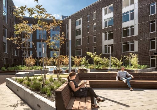 Person sitting reading on bench in sunlit courtyard