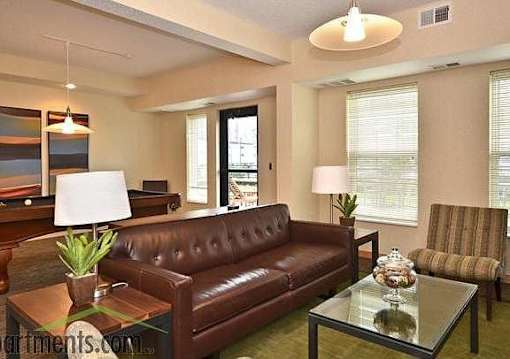 A brown leather couch sits in a living room with a glass table in front of it.