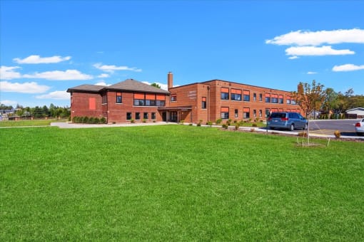 The brick exterior, parking lot, and large green space at Muskego School Apartments