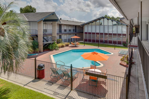 A pool with a sun lounger and umbrella in the foreground with a building in the background.