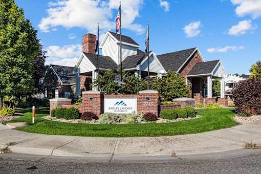 Entrance to community with welcoming flags, mainucured greenery, and building signage at Eagles Landing, Ammon
