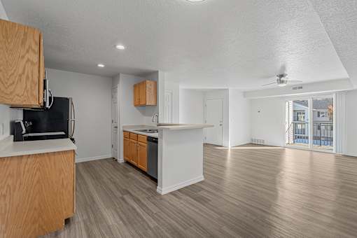 View of expansive living room and kitchen area with plank flooring, natural light, and a sliding glass dooes that lead to a patio or balcony at Eagles Landing, Idaho, 83406