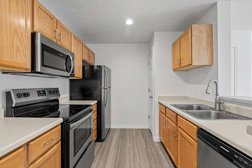 Kitchen area with wooden-style cabinets, plank flooring, sleek appliances, and recessed lighting at Eagles Landing, Ammon, ID, 83406