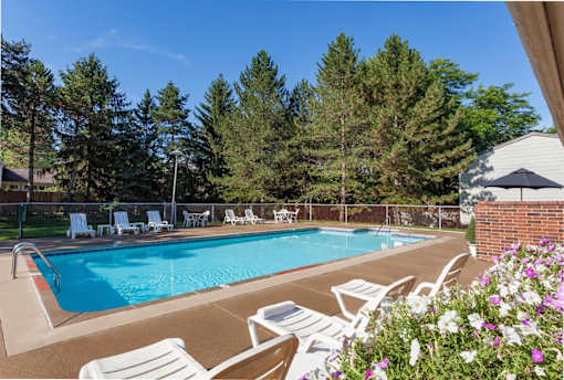 A pool surrounded by trees and chairs.