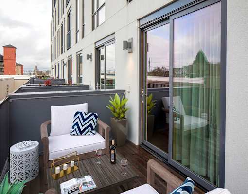 A balcony with a white chair and a table with a bottle of wine on it at The Fitz Apartments, OR 97210