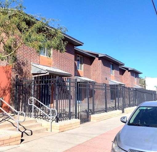 A brick building with a black iron fence and a silver car parked in front.