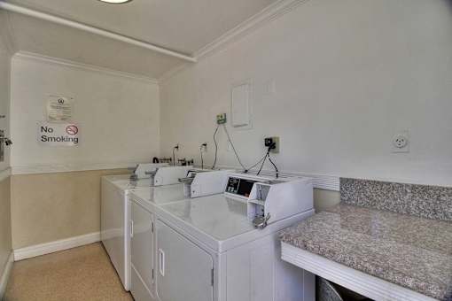 a laundry room with three washing machines and a counter with a sink