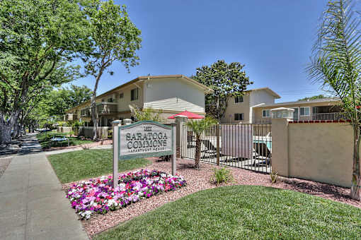 The image shows a sign for Saratoga Commons with a building in the background and a garden in the foreground.