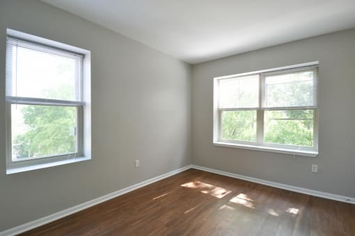 an empty room with two windows and a hardwood floor