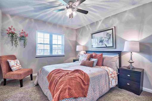 An apartment bedroom with a bed, chair, and ceiling fan.