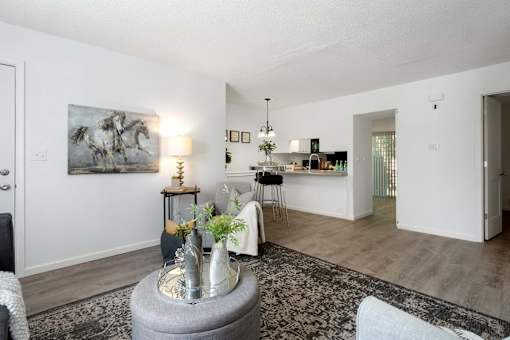 A living room with a grey ottoman and a grey and white patterned rug.