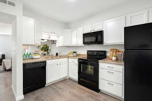 A black refrigerator sits in a kitchen with white cabinets and a black oven.