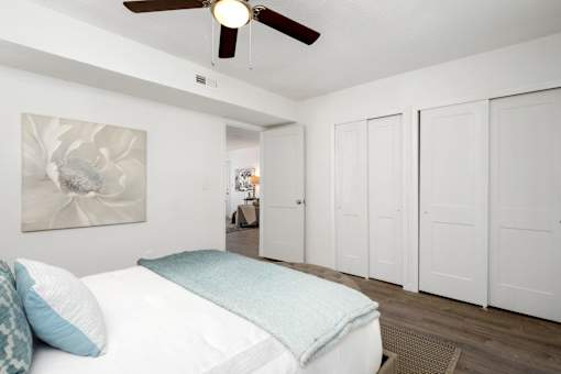 A bedroom with a bed, pillows, a ceiling fan, and a painting on the wall.
