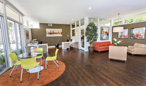 The leasing and managers office has a lounge area with an orange color sofa, two beige guest chairs and coffee table. A round glass table with four apple green guest chairs, a white coffee bar and TV.