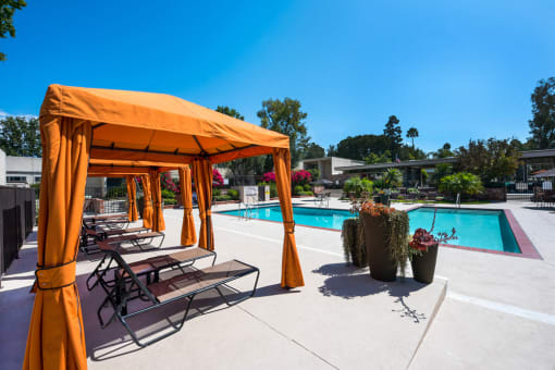 The pool area has three apple green color fabric cabanas, with white seating inside the cabanas. Grey and silver chaise lounges through out the pool deck. A large swimming pool and a jacuzzi.