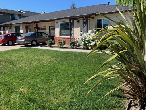 Beautiful side glance of the home, a beige house  with white flowers in front with brick wall siding and a two car driveway the front view of Prodesse Property Group 1617 Union Avenue Redwood City, CA