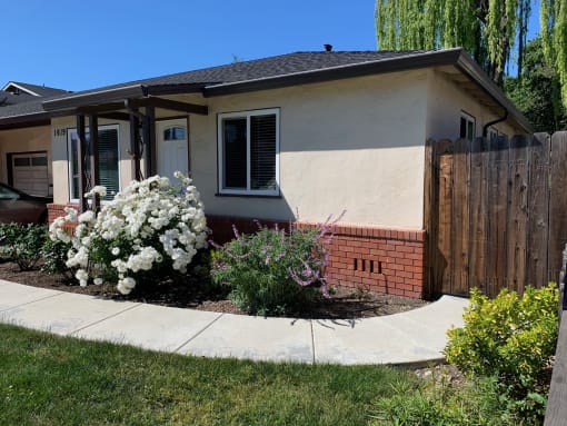 A beige house with a brick wall siding and fence entrance a green lawn and walkway leading to the entrance of Prodesse Property Group 1617 Union Avenue Redwood City, CA 94061 