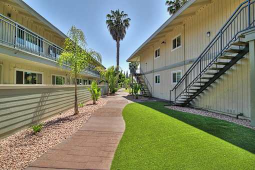 A long, narrow walkway with a grassy area on one side and a building on the other.