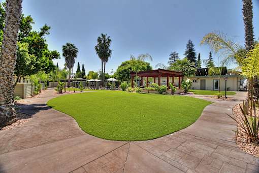 A courtyard with a green lawn and a red building in the background.