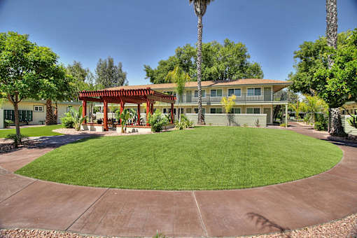 A building with a red roof is surrounded by a green lawn and trees.