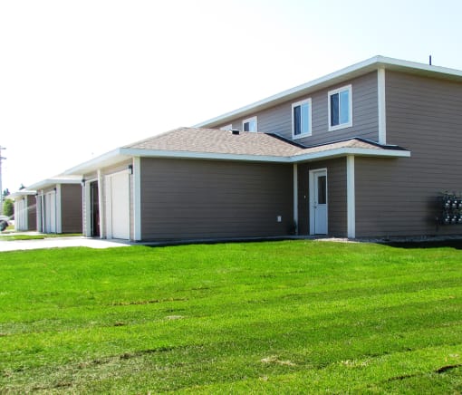 A grey house with a brown roof and a green lawn in front.
