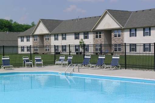 A swimming pool in front of a building with chairs around it.