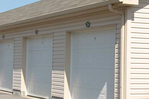 Three white garage doors on a tan building.