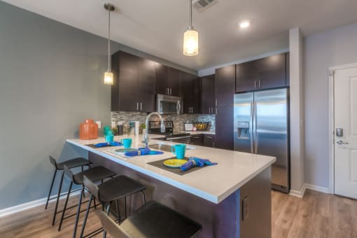 a kitchen with a large island with a sink and three stools  at EdgeWater at City Center, Lenexa