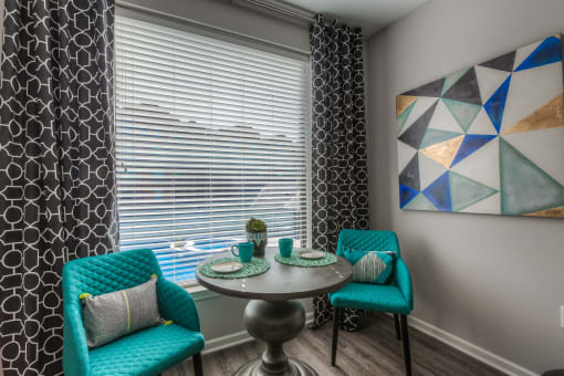 a small dining table with two blue chairs and a large window with blinds  at EdgeWater at City Center, Lenexa, KS