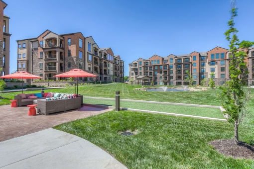 a grassy area with couches and umbrellas in front of an apartment complex  at EdgeWater at City Center, Lenexa, KS
