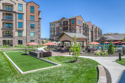 a grassy area with umbrellas and tables and chairs in front of an apartment building  at EdgeWater at City Center, Lenexa, Kansas