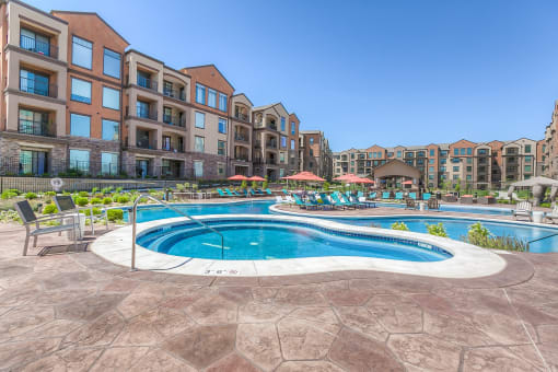 a swimming pool with lounge chairs and umbrellas in front of an apartment building  at EdgeWater at City Center, Lenexa, 66219