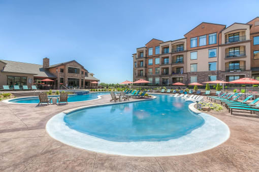 a swimming pool with lounge chairs and umbrellas with a resort style building in the background  at EdgeWater at City Center, Lenexa