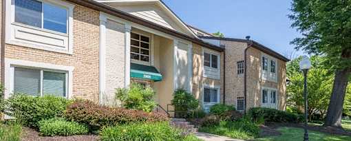 A building with a green awning is surrounded by bushes and trees at Potomac Ridge Apartments, Woodbridge