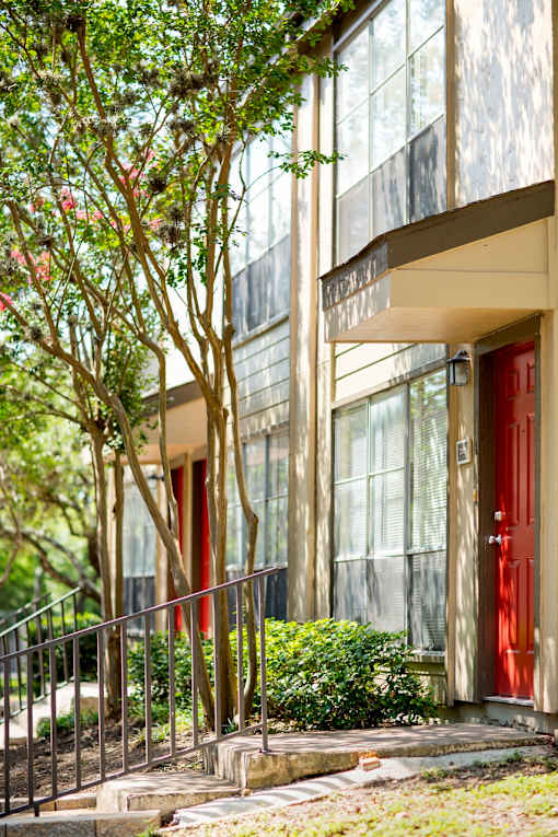 Building entrance with red door and metal railing at The Colony Apartments, Universal City, 78148